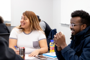 Two students sit at a table and smile looking out of the frame to the left.